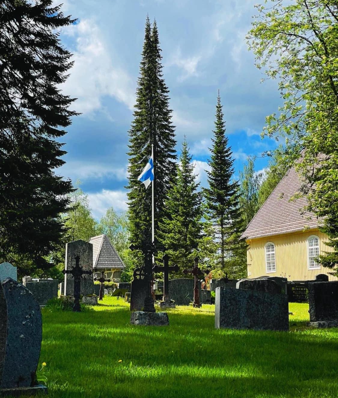 Keltainen kirkko, hautausmaa ja kirkkopuisto, kesäkuva. Suomen lippu salossa.