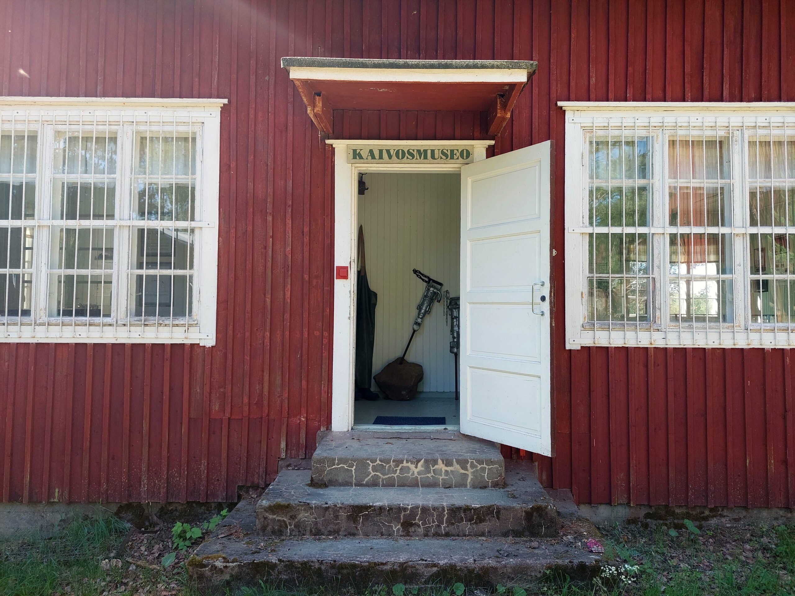 Punainen, puinen museorakennus ovi avoinna.