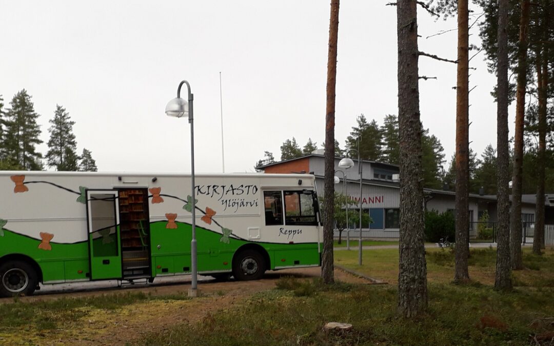 Vihreävalkoinen kirjastoauto pysäkillä päiväkodin pihassa mäntymetsässä.